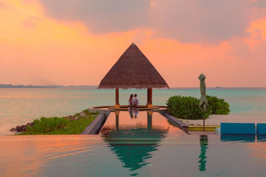 A couple enjoying a romantic moment by the sea and pool under a beach cabana during sunset Maldives