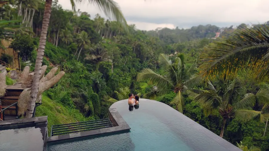 A couple relaxes in a luxurious infinity pool with a breathtaking view of Bali lush jungle