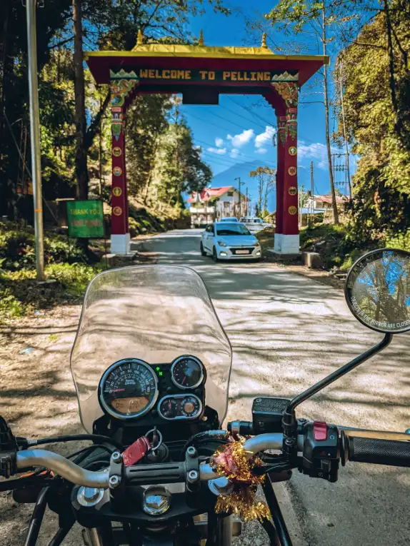 A motorcycle rides through the Welcome to Pelling gate surrounded by lush trees